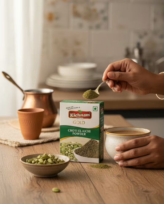 Person adding Kichham Gold Chotti Elaichi powder to a cup in a kitchen setting.