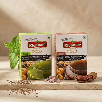 Two boxes of Kichnam Gold golgappa masala spices on a wooden surface with ingredients.