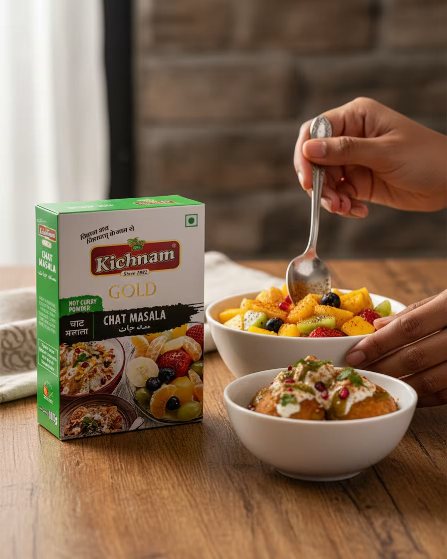 Kichham Gold Chat Masala box with a bowl of food and a hand holding a spoon on a wooden table.